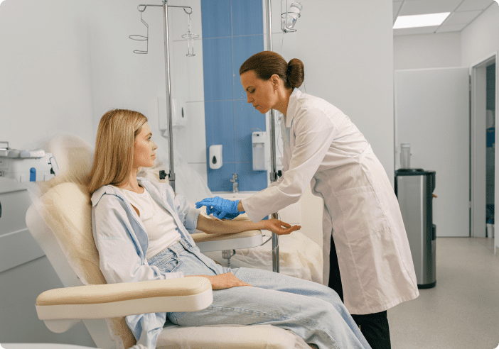 A healthcare professional administers an IV to a seated person in a medical setting.