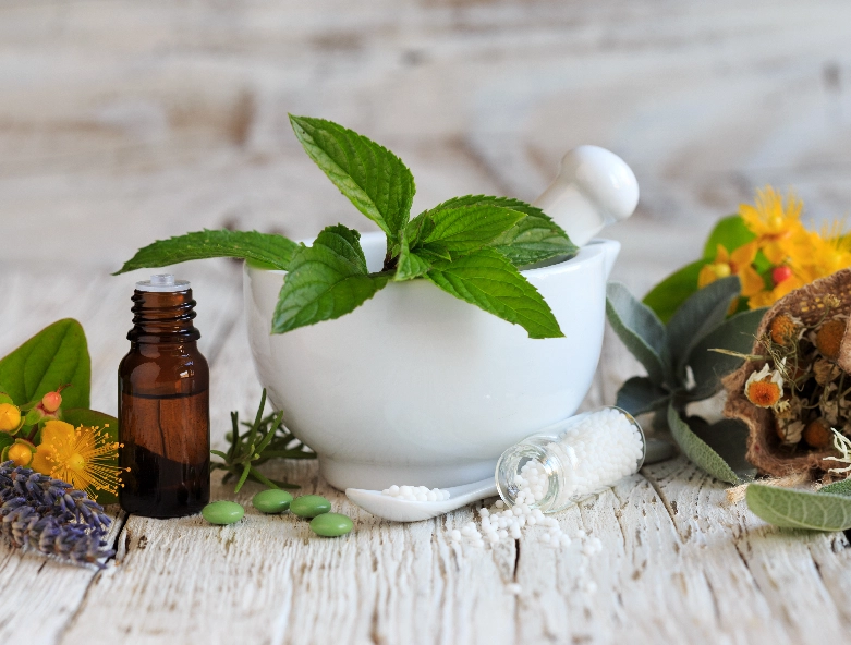 A mortar and pestle with herbs in it next to an oil bottle.