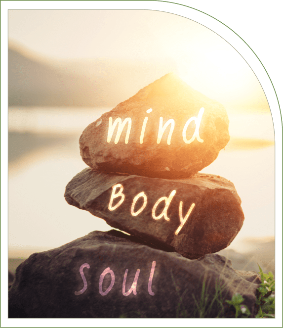 Three stacked rocks with text "mind," "body," and "soul" in a serene outdoor setting with soft sunlight.